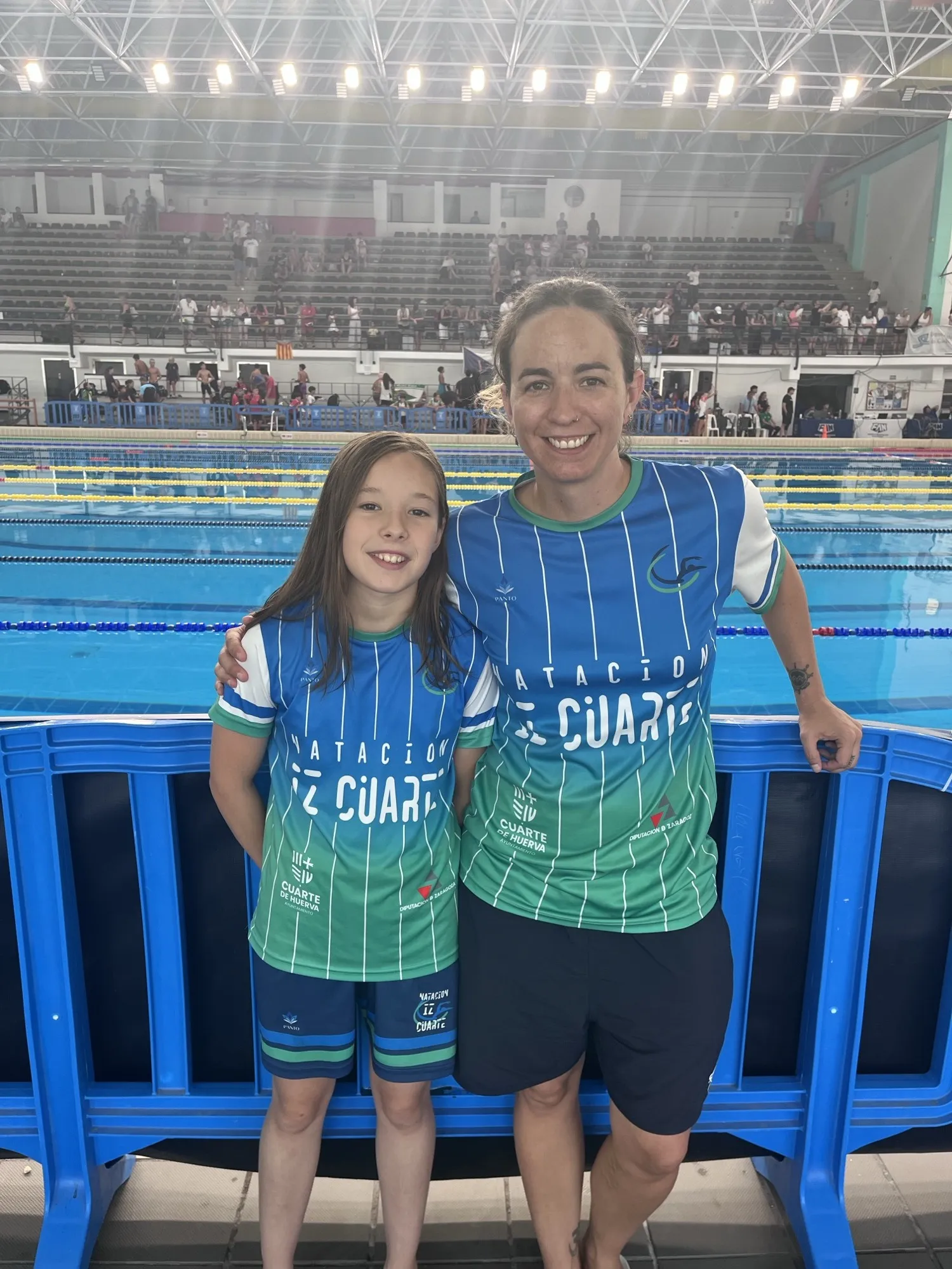 Vega Moreno junto a su entrenadora, apoyadas en la valla de la piscina donde se disputó el Campeonato de España Alevín