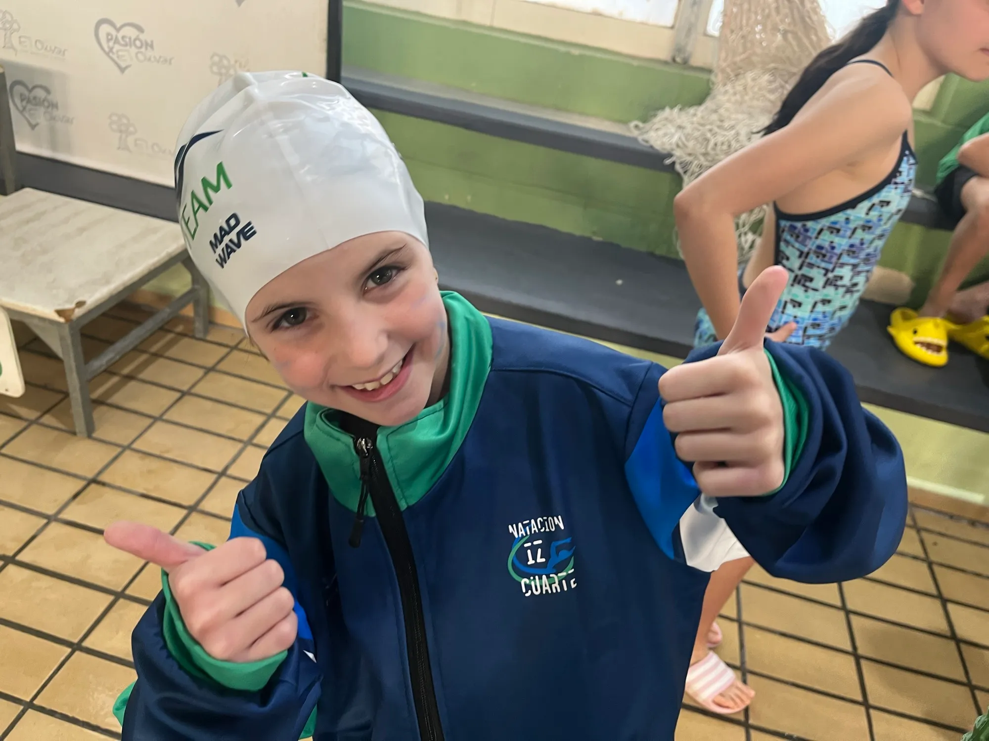 Nadadora del club sonriendo con el gorro y el chándal del equipo.