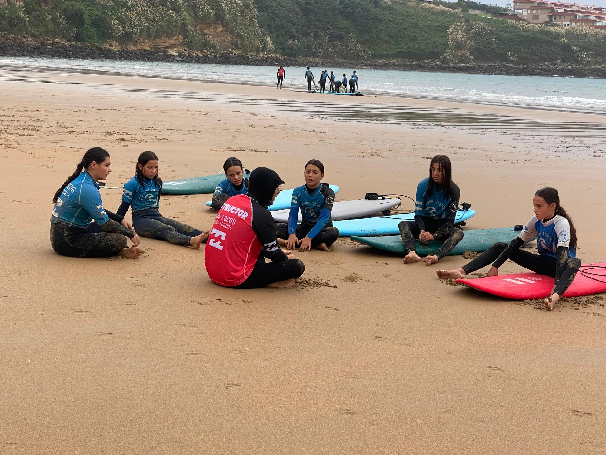 Nadadores del Club Natación IZ Cuarte sentados en la playa escuchando las explicaciones de su instructor de surf